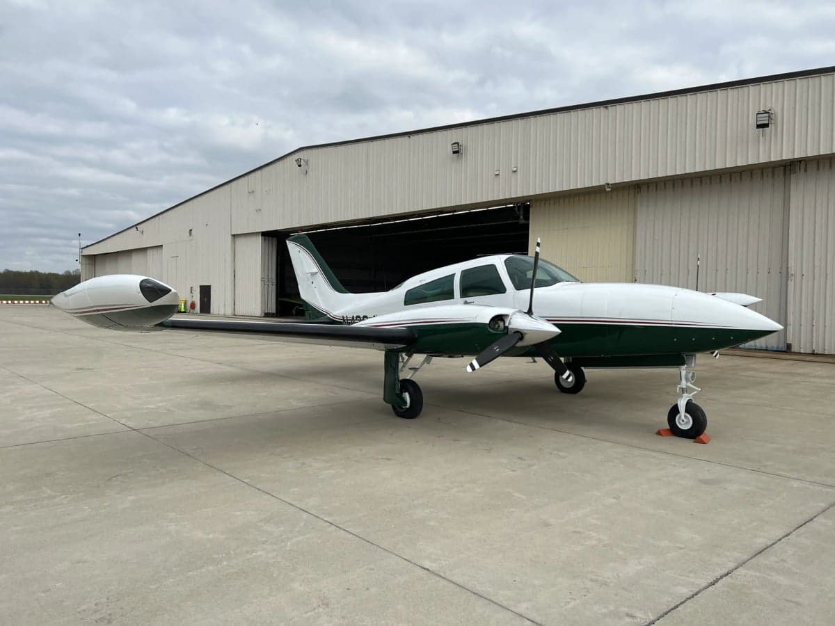 N4264J is a white and green Beechcraft Bonanza parked in front of a hangar.