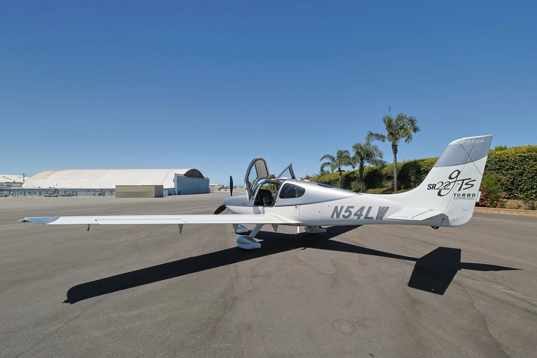 Three-quarter rear view of a silver and white Cirrus SR22T (N54LW) with both doors open, parked on an tarmac.