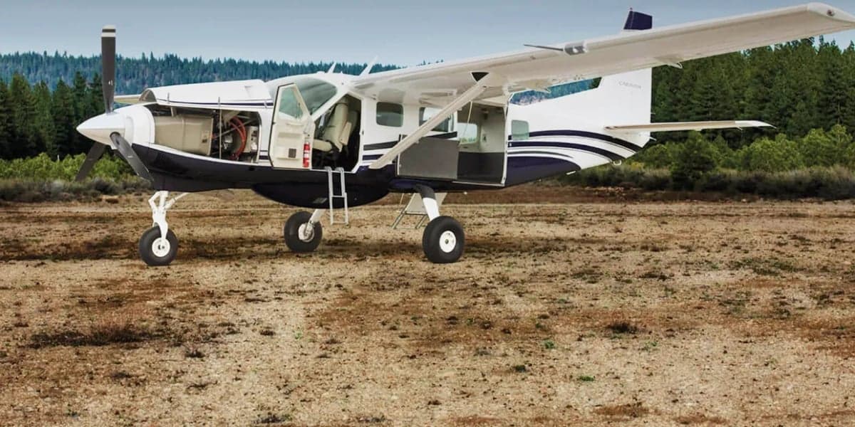 A white and blue Cessna Caravan is parked on a dirt field with its doors open.