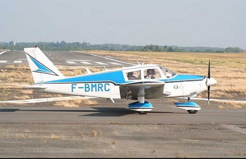 A white and blue light aircraft, F-BMRC, with two people inside, on a runway.