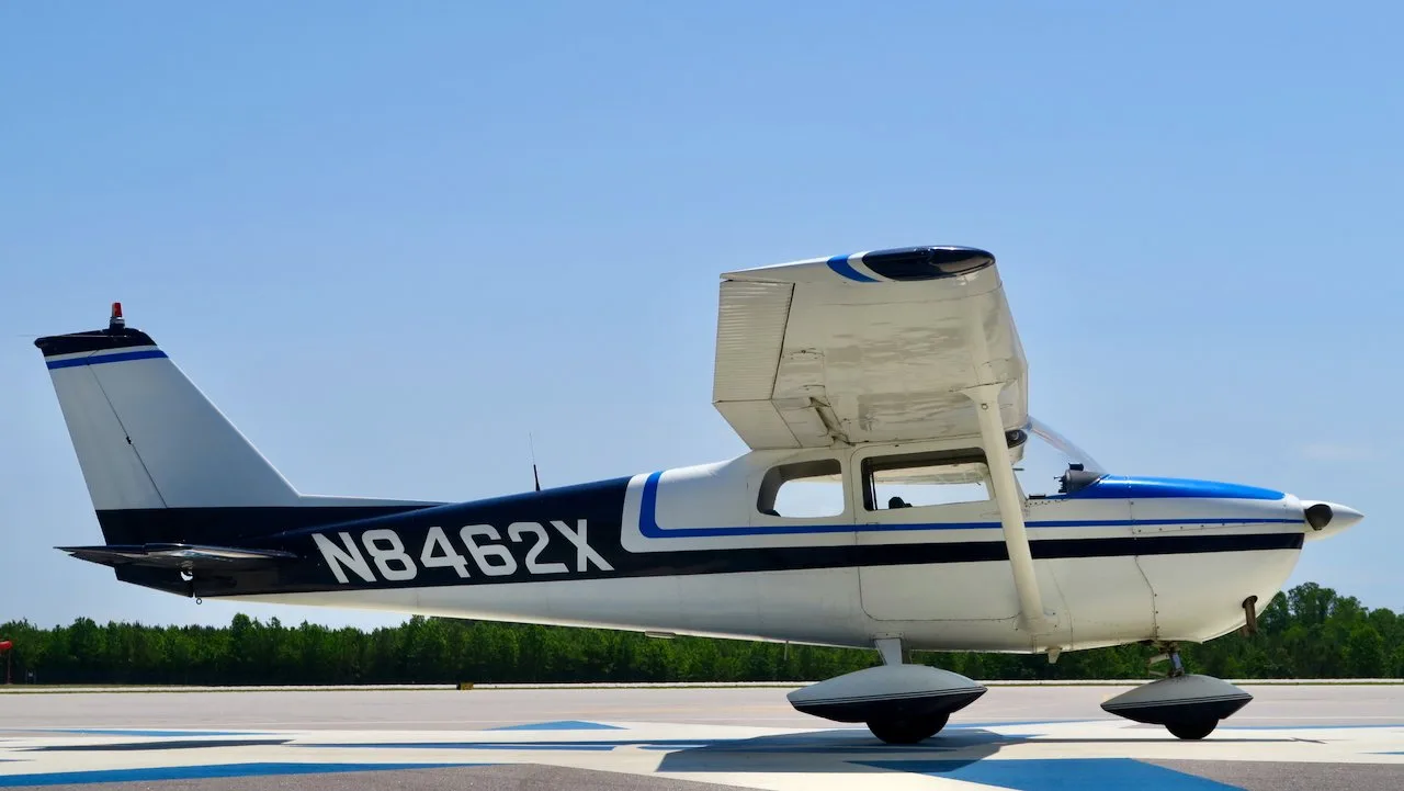 A side view of a white Cessna 172 with blue and black stripes, N8462X, parked on an airfield.