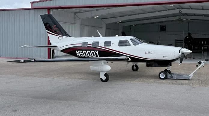 A white and maroon M350 aircraft with registration N500DY is parked in front of a hangar.