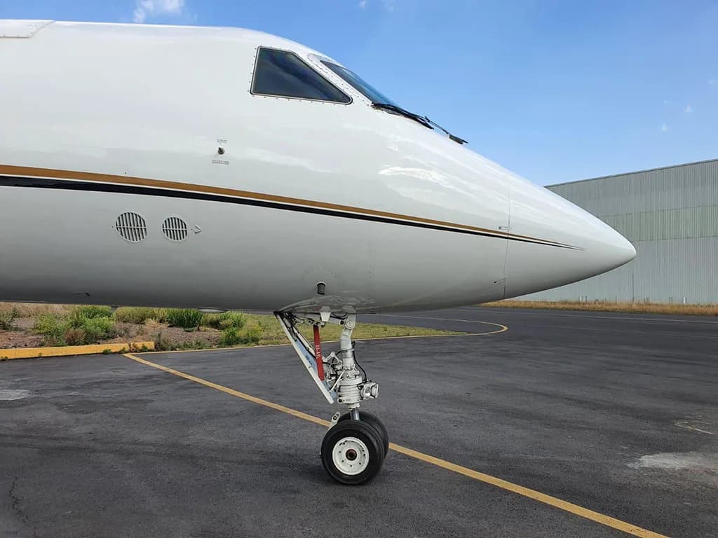 A close-up view of the nose and front landing gear of a white business jet with gold and black stripes.