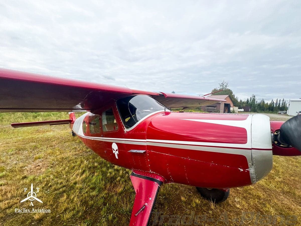 A close-up view of the front-left side of a red and silver single-engine aircraft with a skull logo on the fuselage.