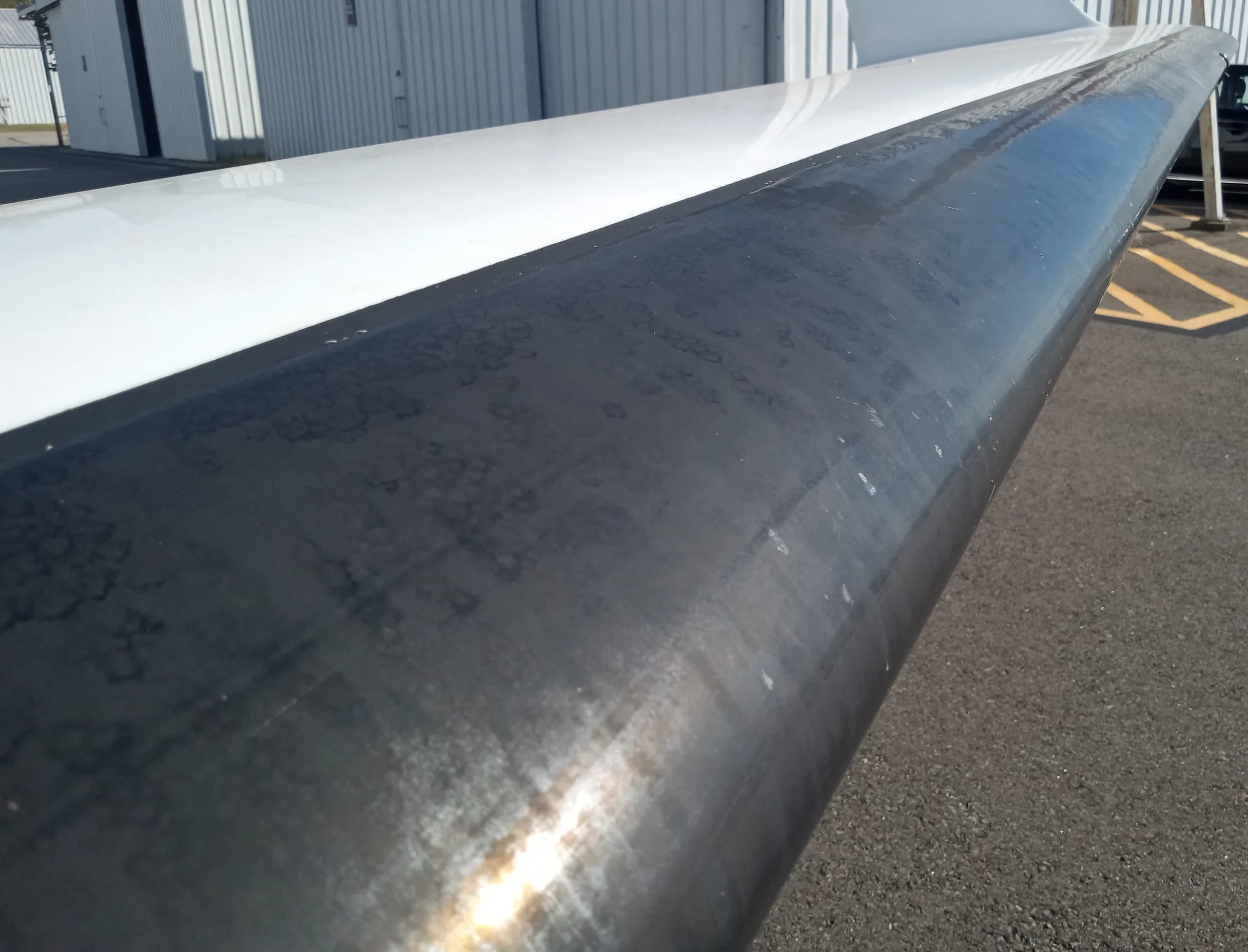 A close-up view of the dark leading edge of an aircraft wing, showing some wear.