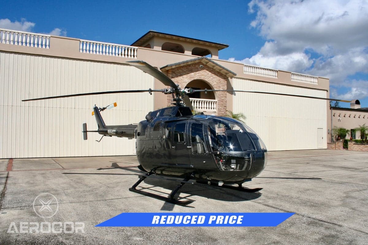 Front three-quarter view of a black helicopter (N554RP) parked on an apron in front of a hangar.
