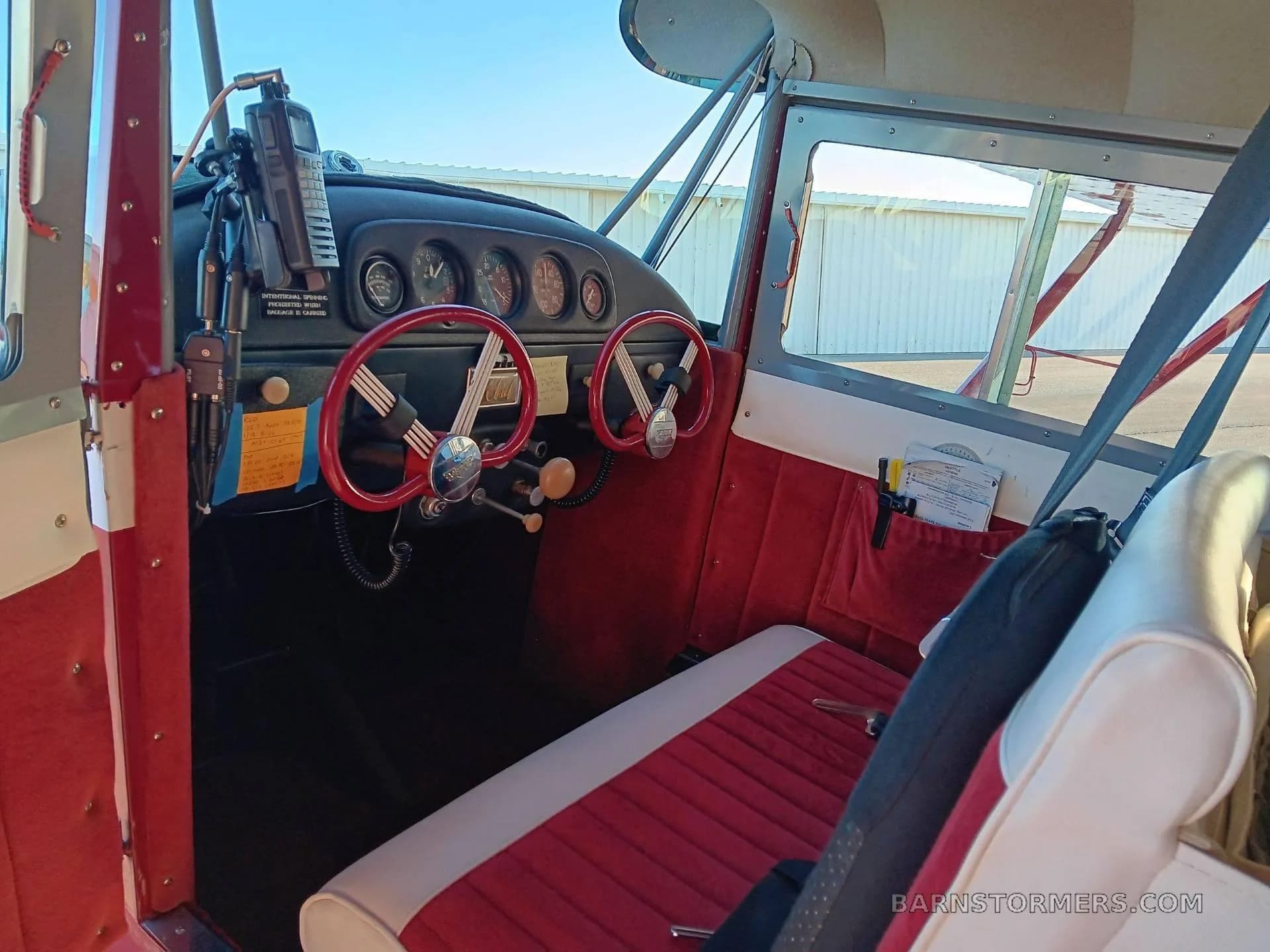 The red and white interior cabin of an Aeronca Chief, showing the seats and part of the instrument panel with red yokes.