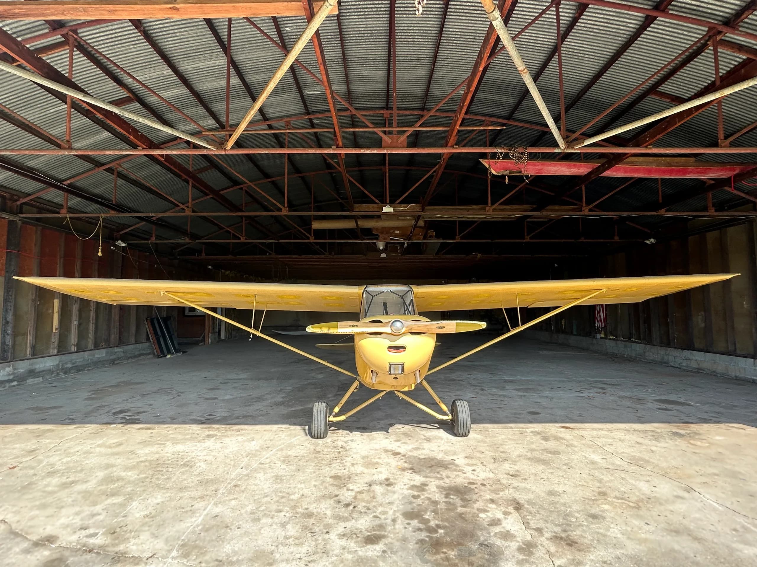 A yellow Aeronca 7AC Champ aircraft with an orange stripe parked head-on inside a hangar.