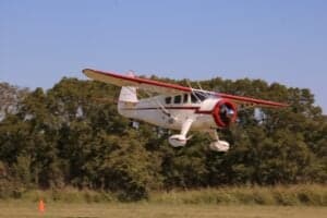 A Howard DGA-15P aircraft is in flight, with trees in the background.