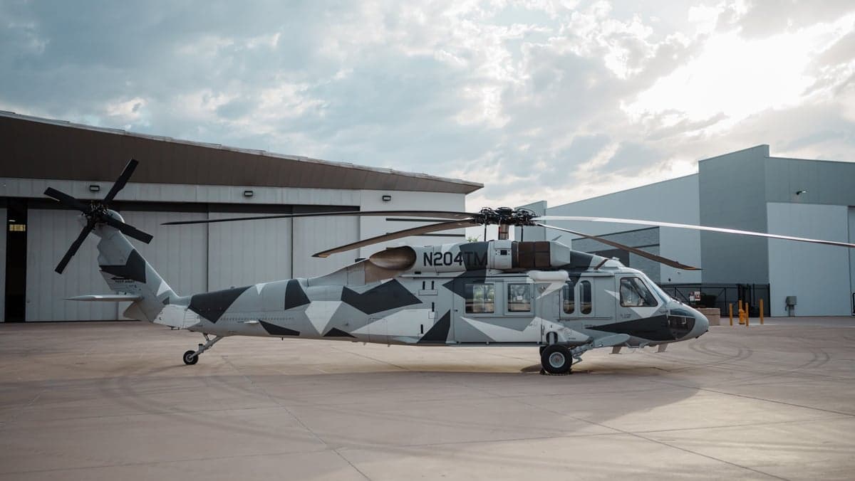 Side view of a Sikorsky S-70i helicopter with a gray camouflage paint scheme on the tarmac.