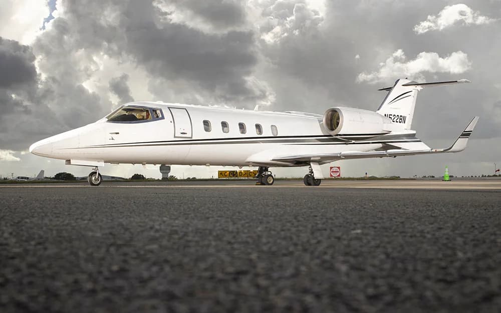 A white Learjet with black and grey stripes, tail number N522BN, parked on a tarmac under a cloudy sky.