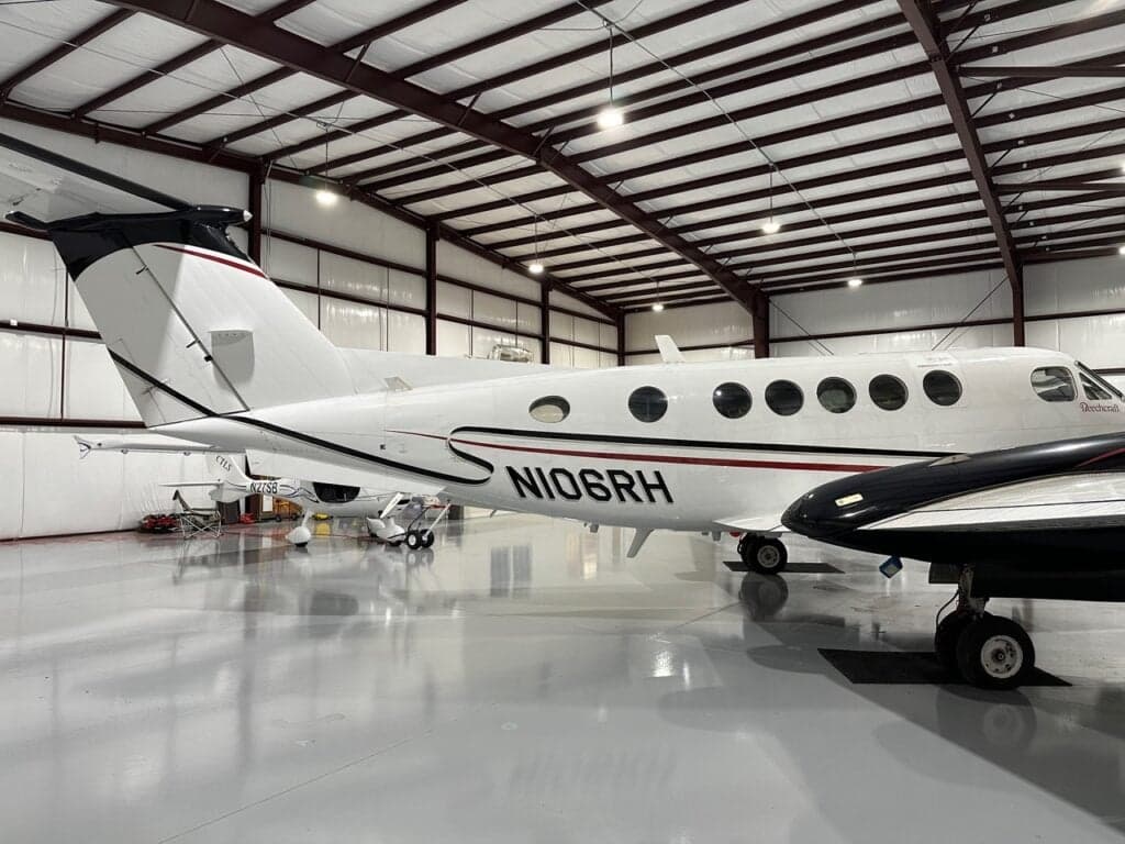 A side view of the white Beechcraft King Air N106RH with black and red stripes, parked in a hangar.