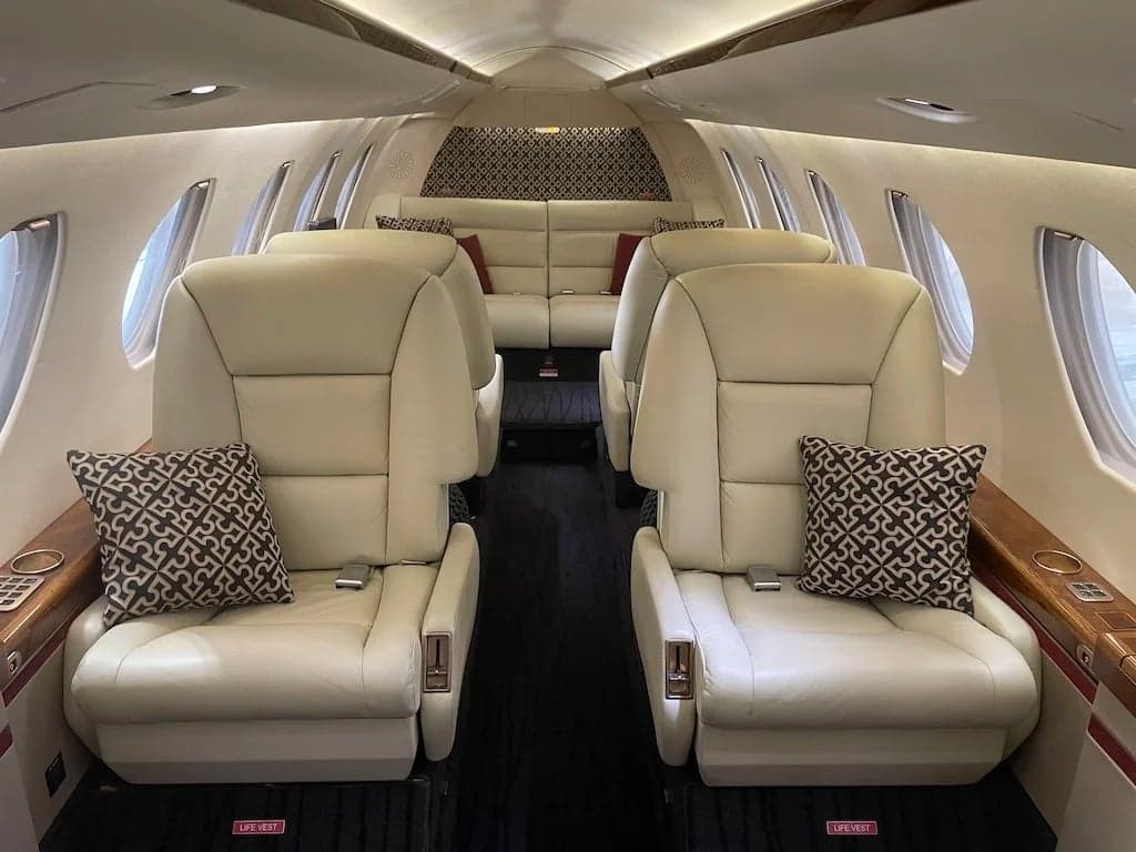 Interior view of the aircraft cabin with cream-colored leather seats and patterned pillows.