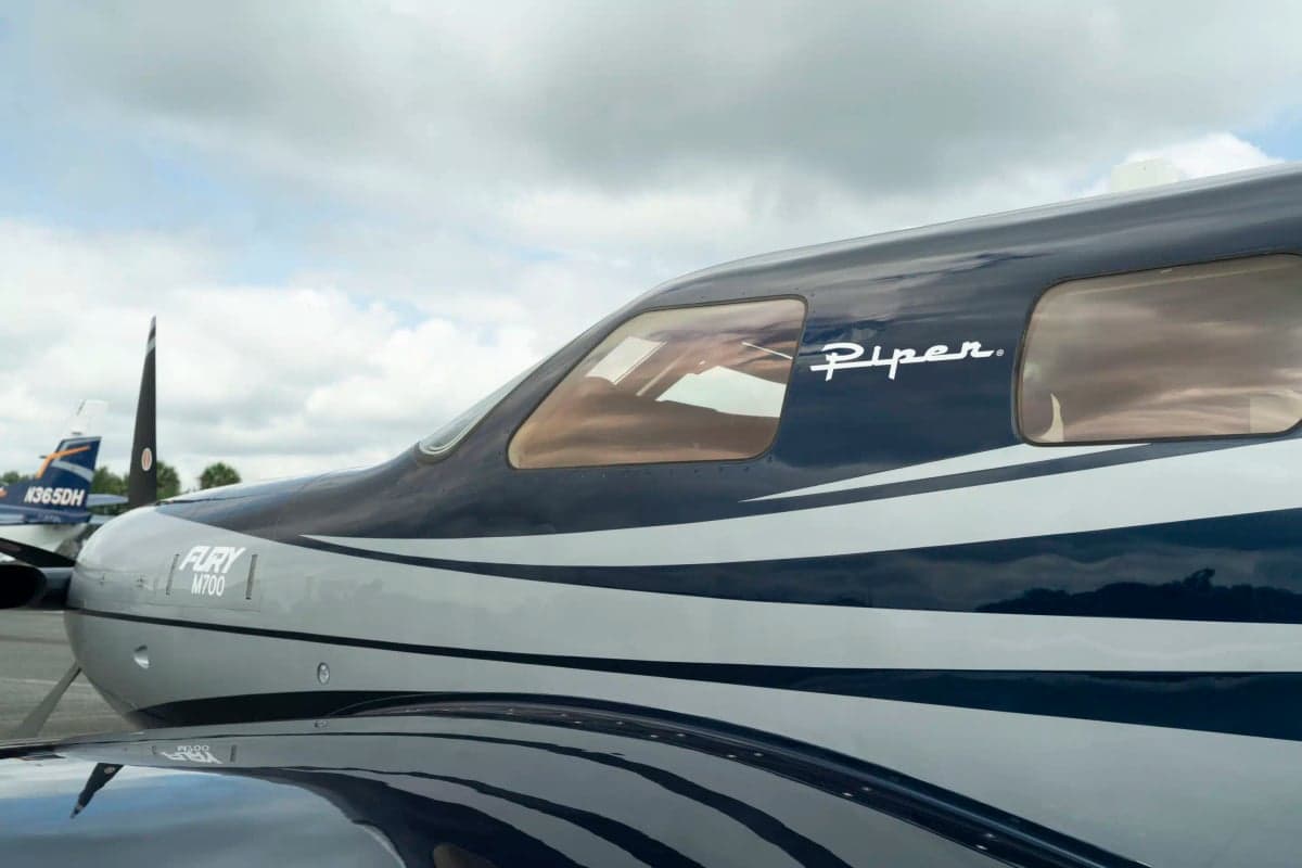 A close-up of the Piper M700 Fury's cockpit windows and front fuselage, showing the 'Piper' logo and 'Fury M700' designation.