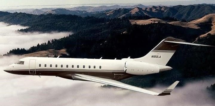 A Bombardier Challenger 300 flying over a mountainous landscape.