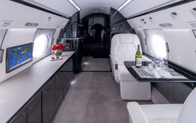 Interior of the aircraft cabin with a sofa, white leather seats, and a table with champagne.