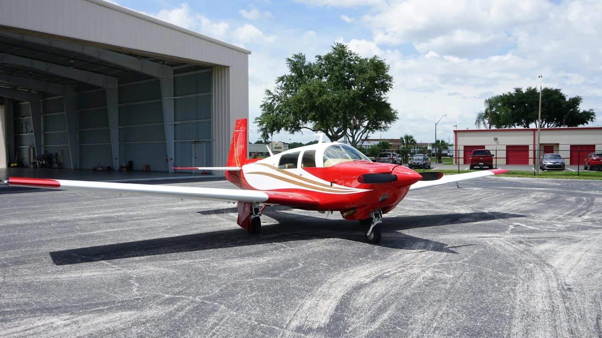 A red and white single-engine aircraft, N33YZ, is parked on an asphalt apron in front of a hangar.