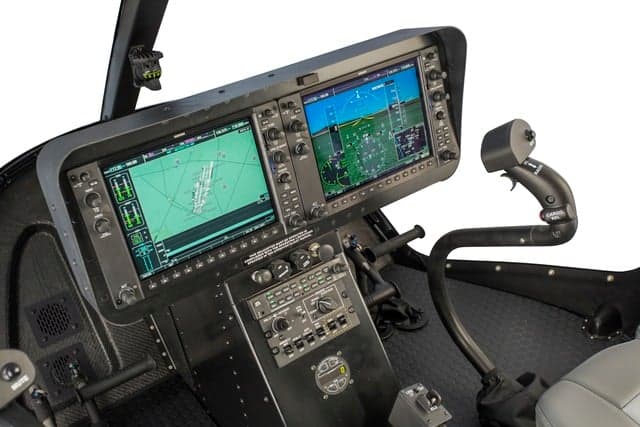Close-up of a helicopter cockpit with dual screens and controls.