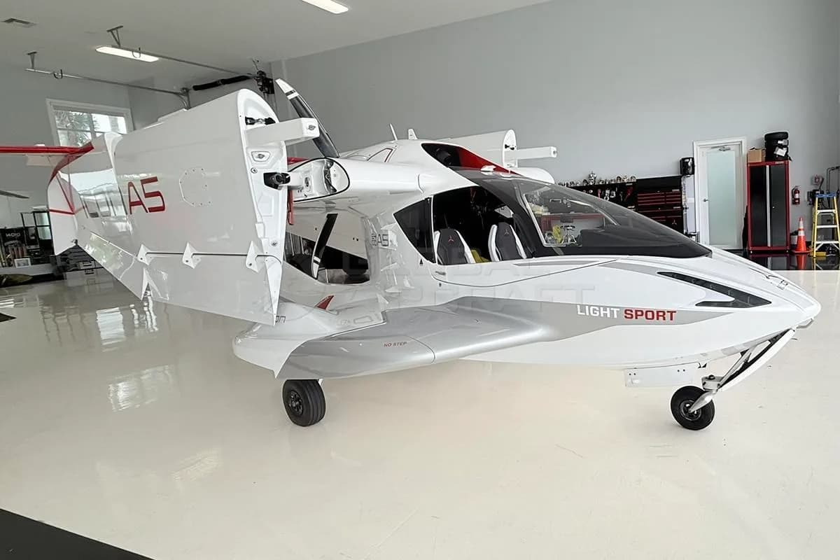Front three-quarter view of a white and red Icon A5 amphibious light sport aircraft with wings folded, inside a hangar.
