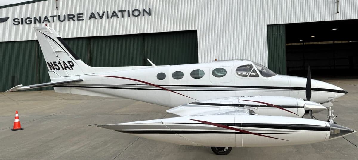 Side view of the Cessna 340A aircraft with registration N51AP parked in front of a Signature Aviation hangar.