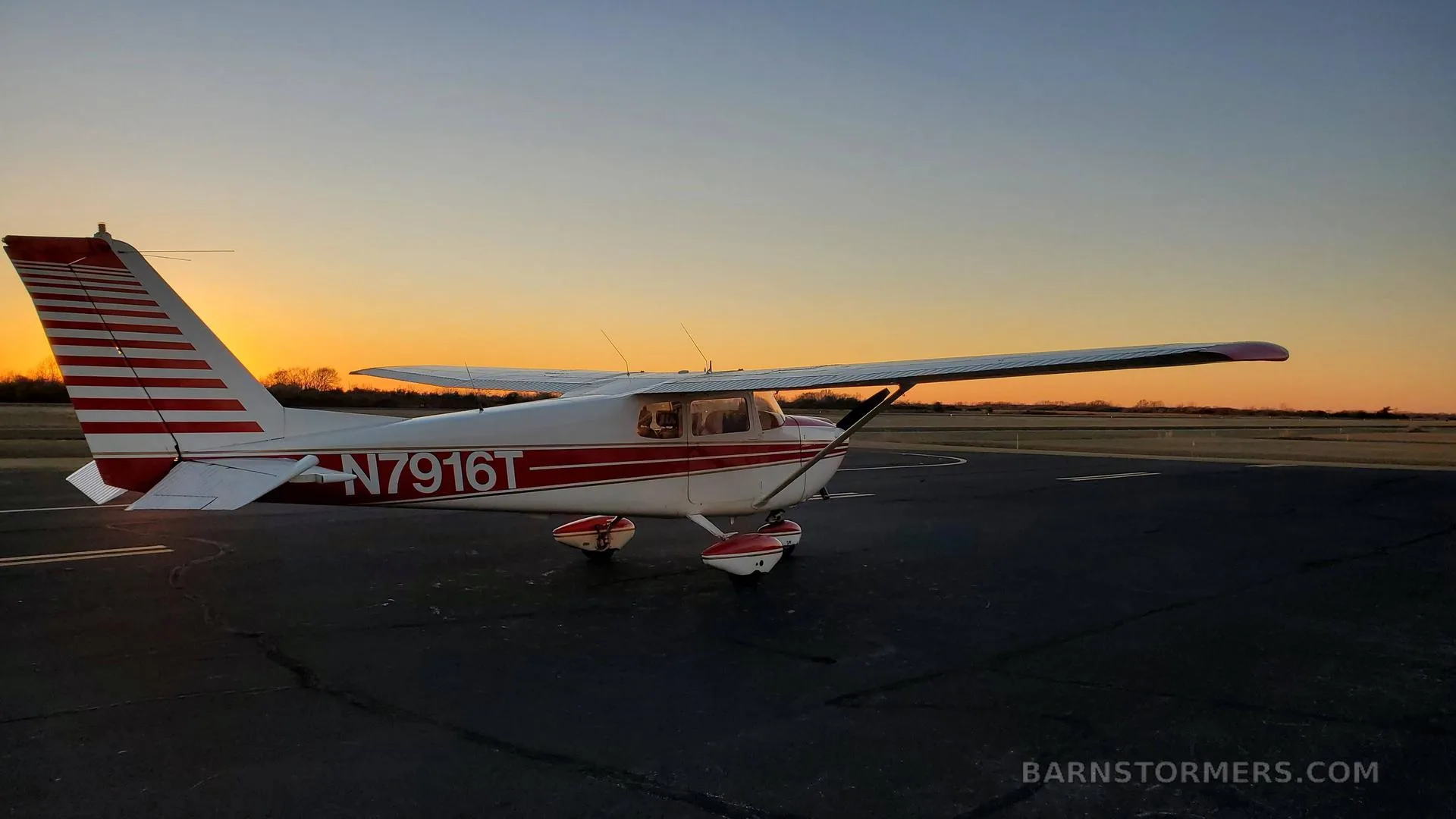 A white and red Cessna 172 with registration N7916T parked on an airfield at sunset, viewed from the rear-left.