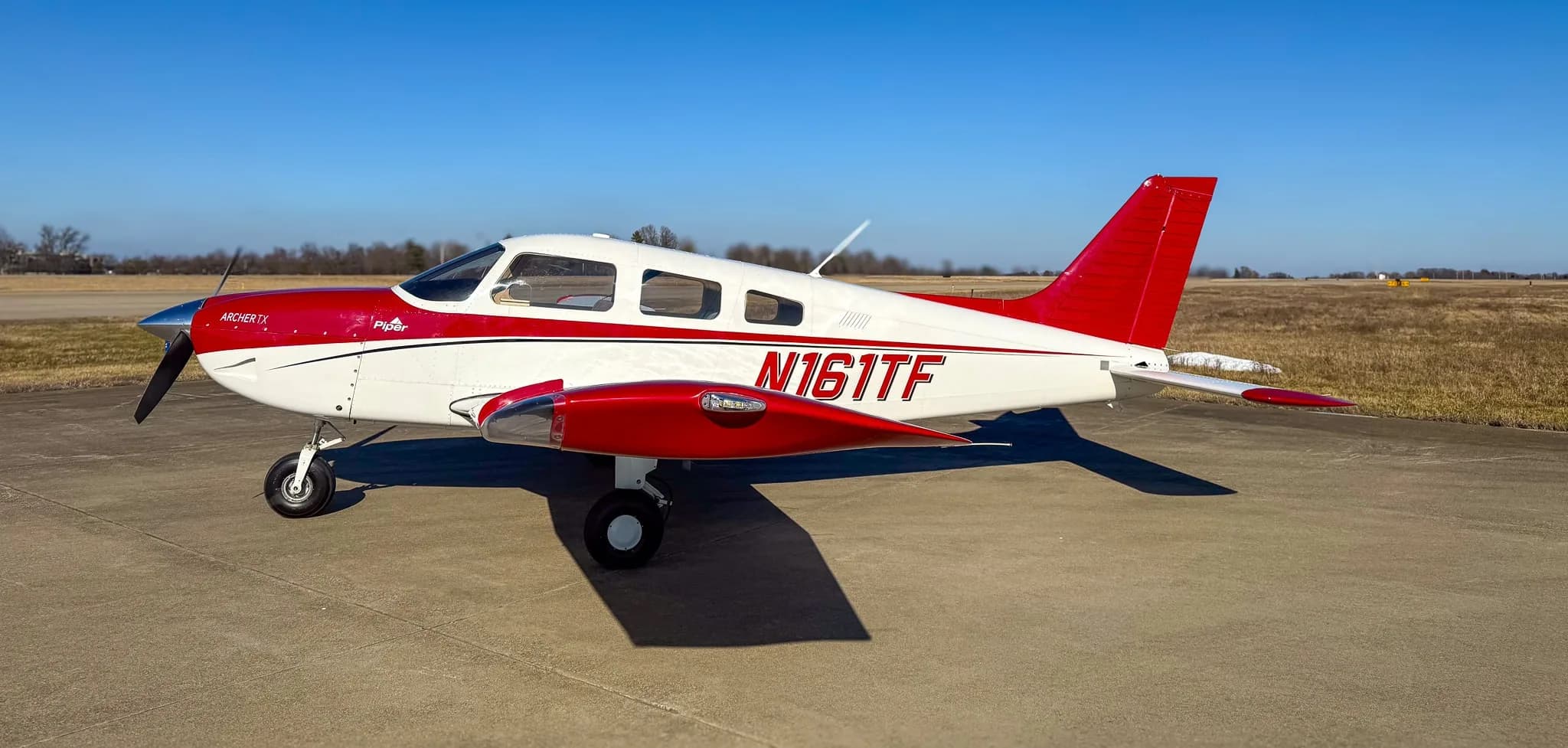 A side view of a red and white Piper Archer TX aircraft, tail number N161TF, parked on an asphalt tarmac.