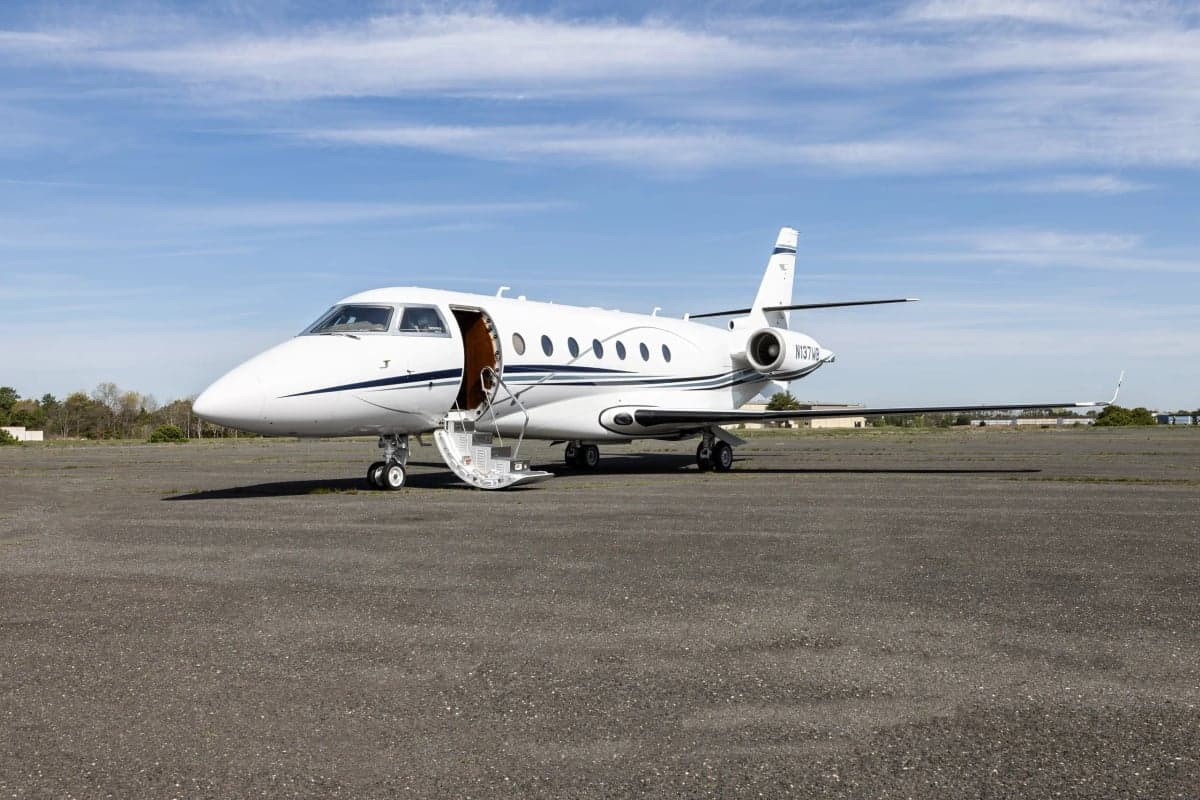 A white Gulfstream G150 aircraft with blue stripes, registration N137WB, is parked on the tarmac with the door open.