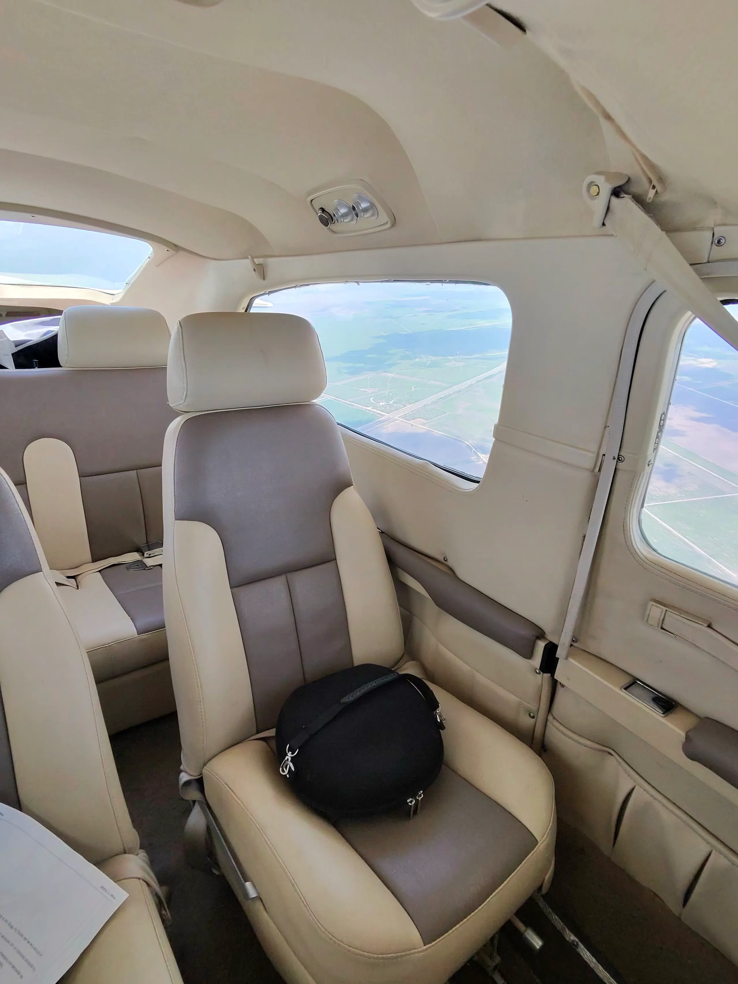 The interior cabin of an aircraft with two-tone beige and grey seats, showing a view of fields from the window.