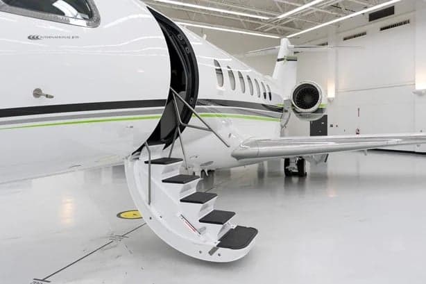 The stairs are extended from the open door of the white jet with green accents.
