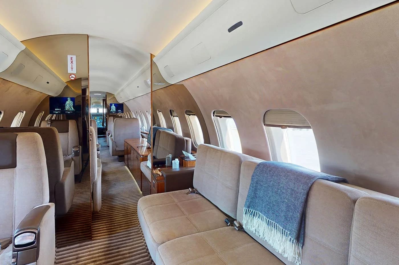 The spacious interior of a private jet, featuring a comfortable beige sofa with a blue blanket and individual seats further down the cabin.