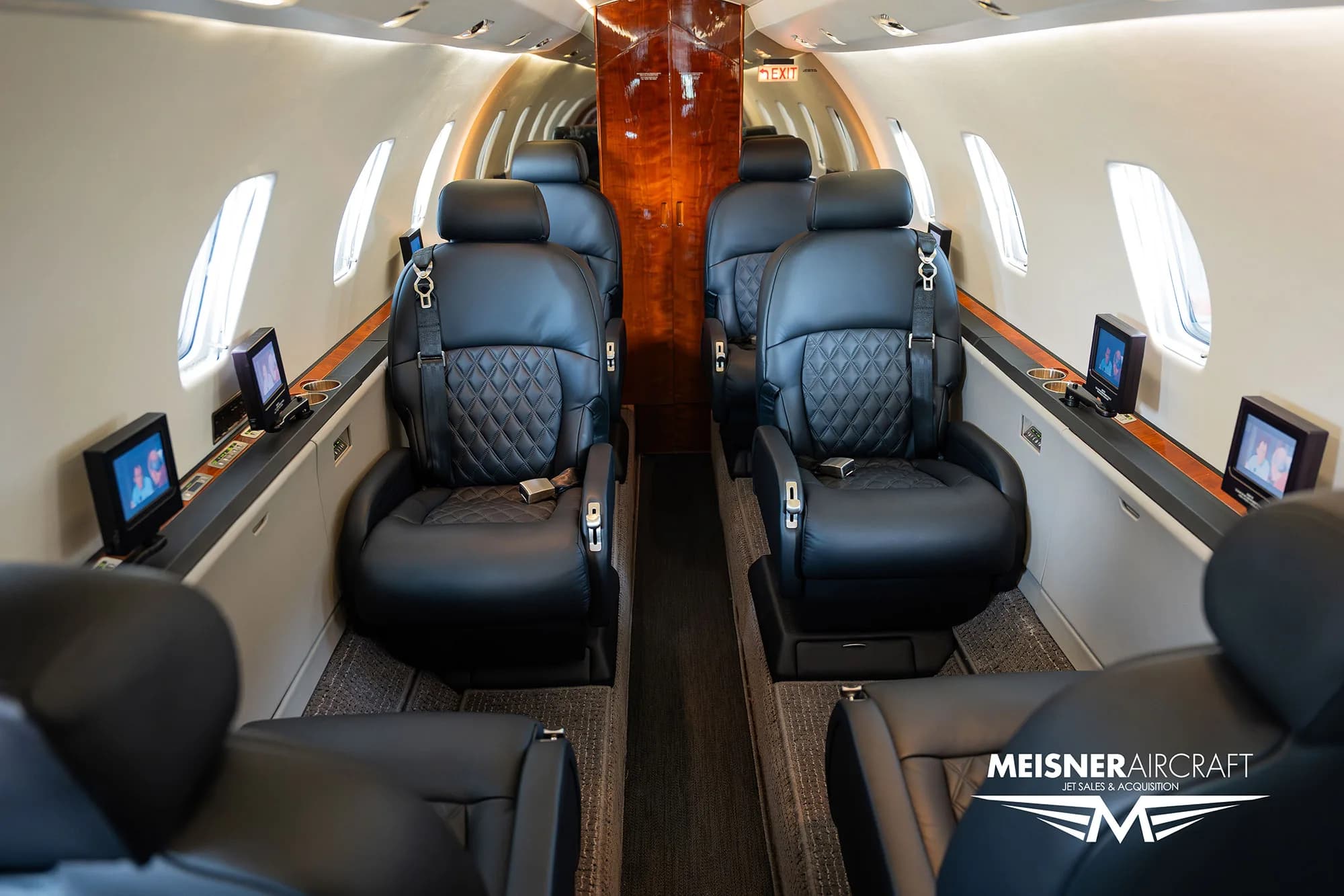 The luxurious interior cabin of a Citation Excel business jet with black leather seats and wood paneling, looking towards the rear.