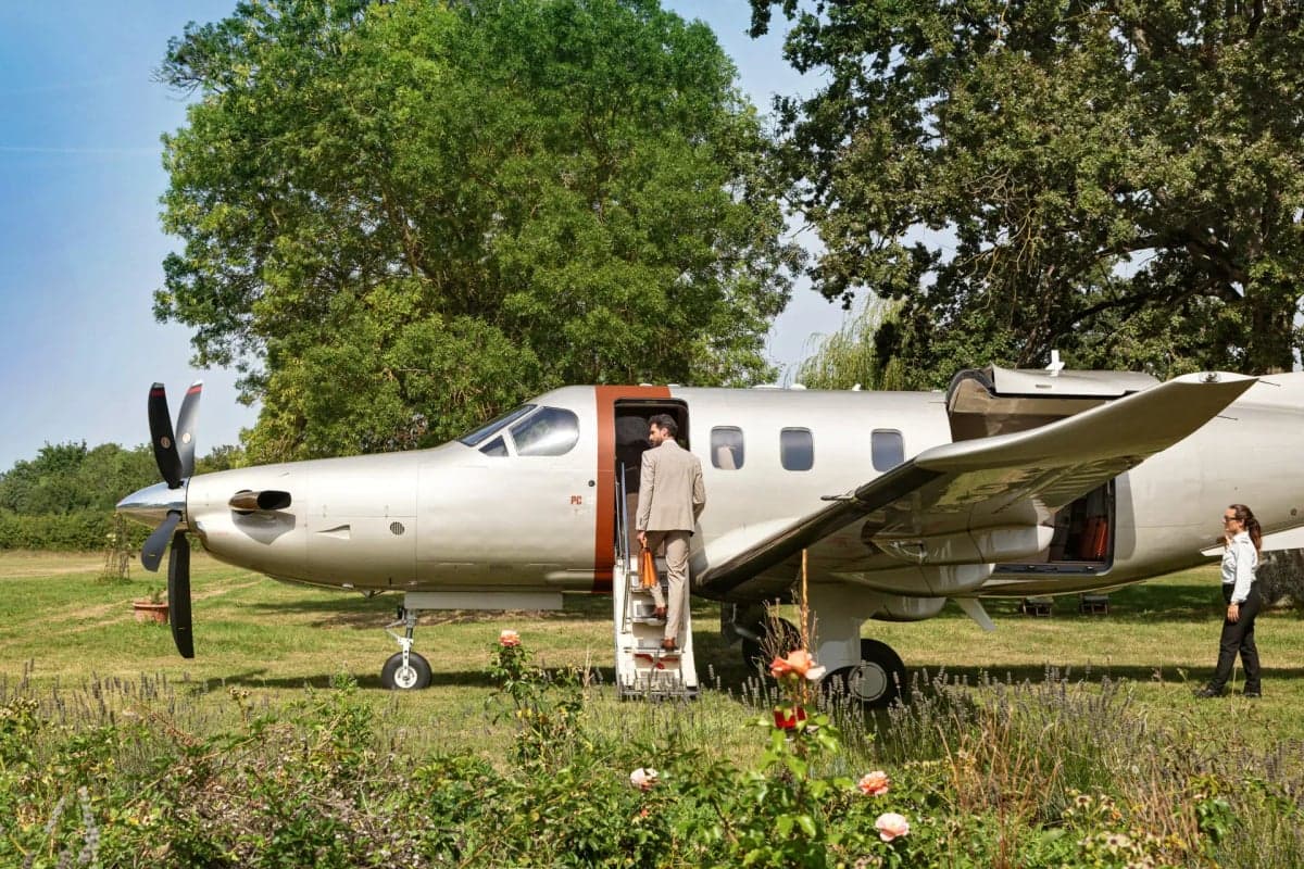 A Pilatus PC-12 aircraft parked on a grassy field with people nearby.