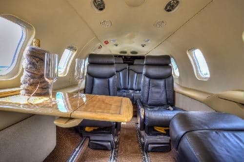 The Learjet 31A cabin features black leather seats and a wooden table with champagne flutes.