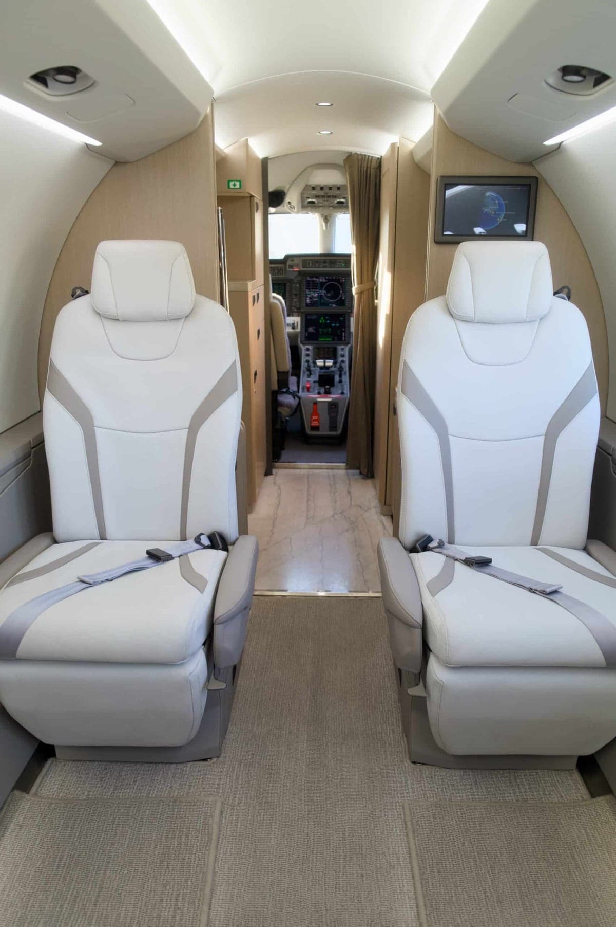 View of the aircraft's interior cabin with white leather seats and a view into the cockpit.