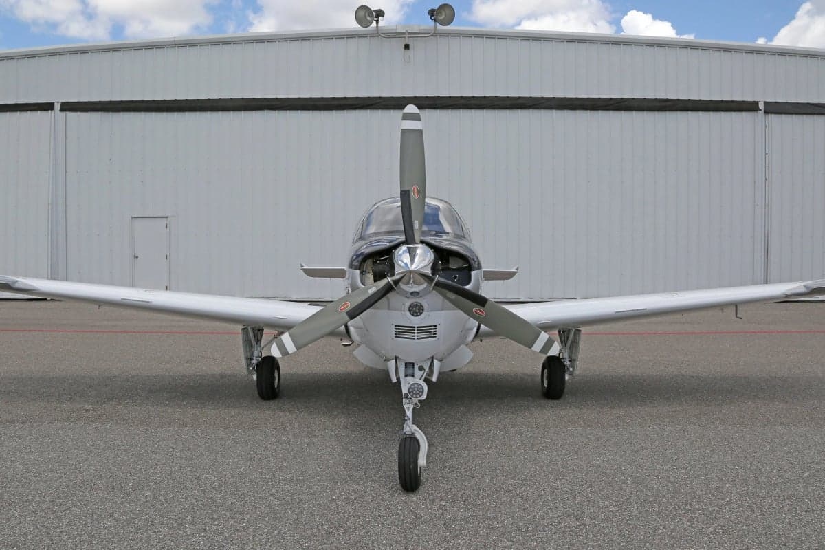 Close-up front view of a Beechcraft Bonanza aircraft parked in front of a hangar.