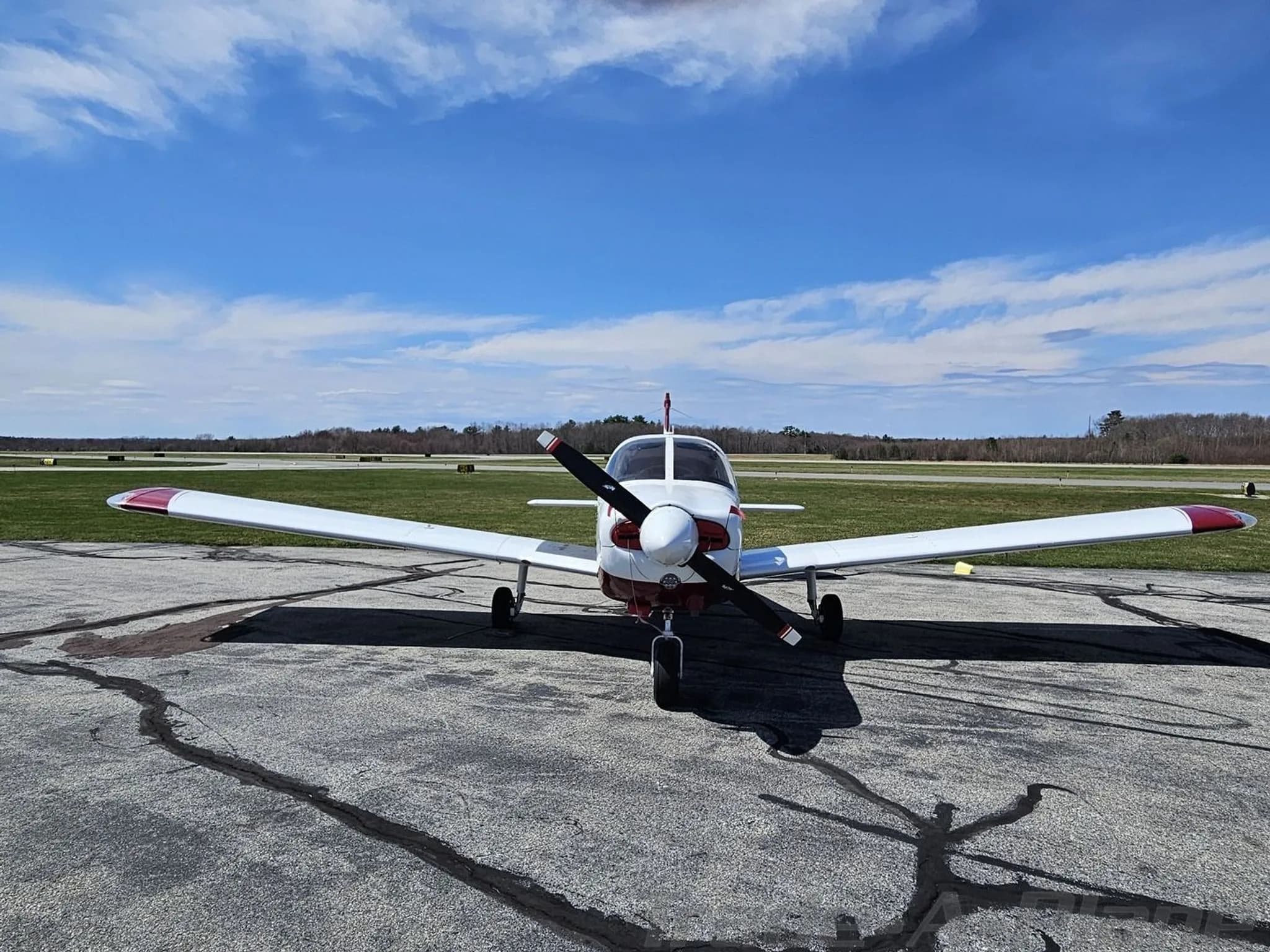 Front view of a white and maroon Piper PA-28 aircraft on an airfield under a blue sky.
