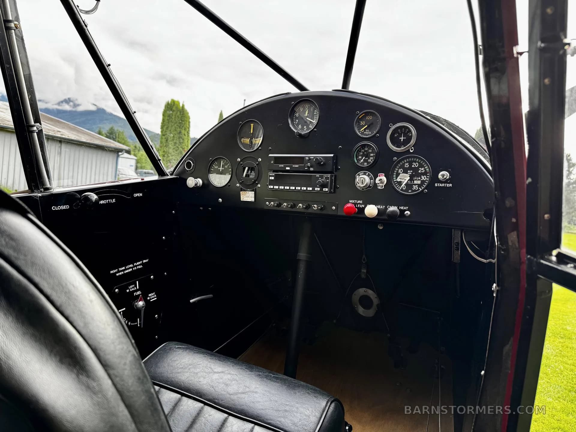 The black instrument panel of a Piper Cub, showing various gauges, radio, and controls from the pilot's perspective.