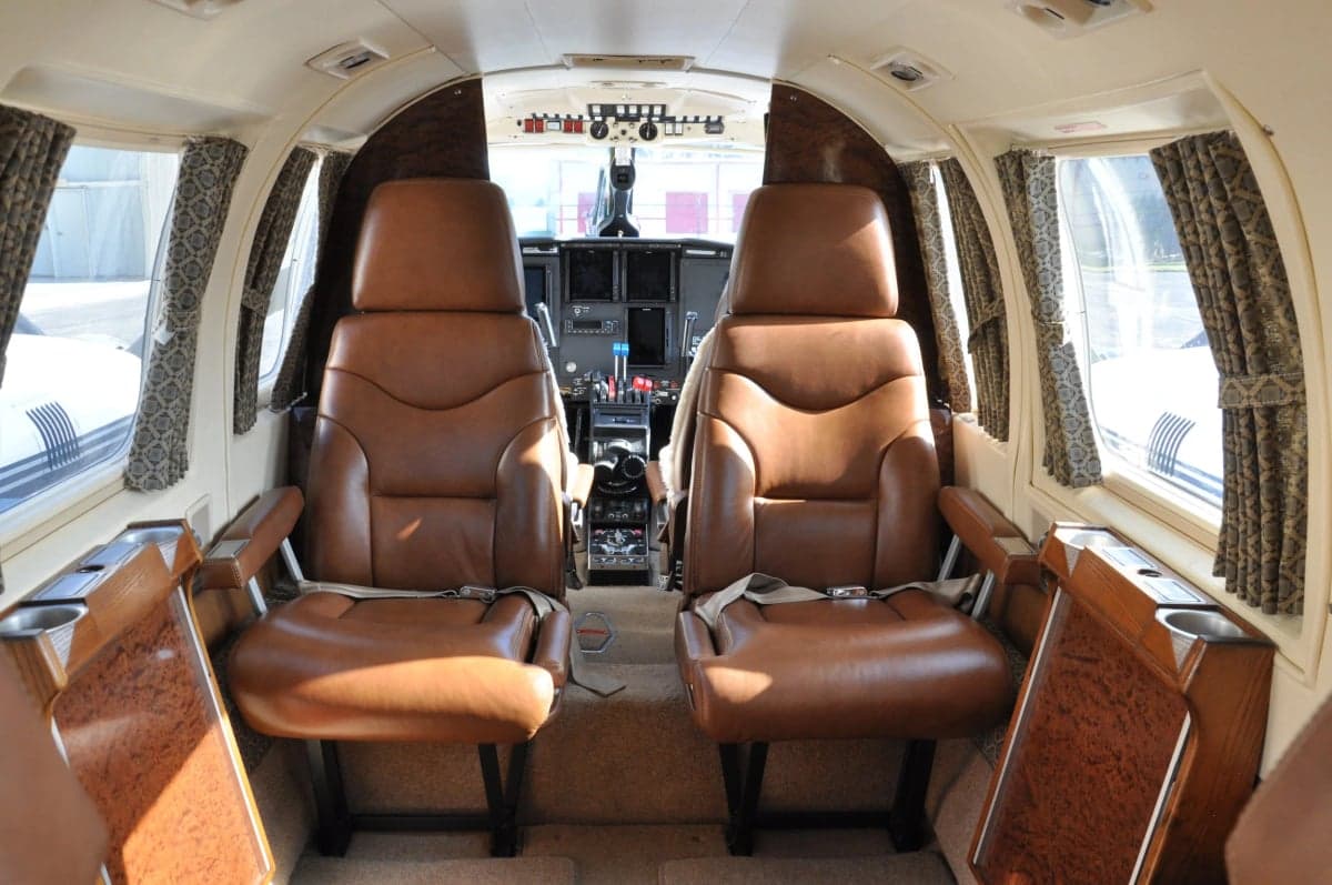 View of the aircraft cabin with two brown leather seats and cockpit in the background.