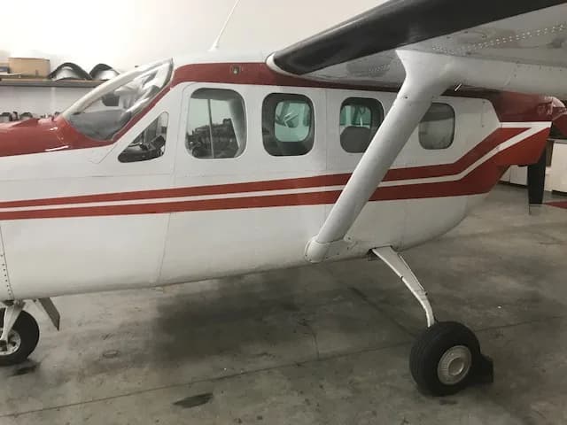 A close-up side view of the fuselage and wing of a white and red Cessna 337 Skymaster in a hangar.