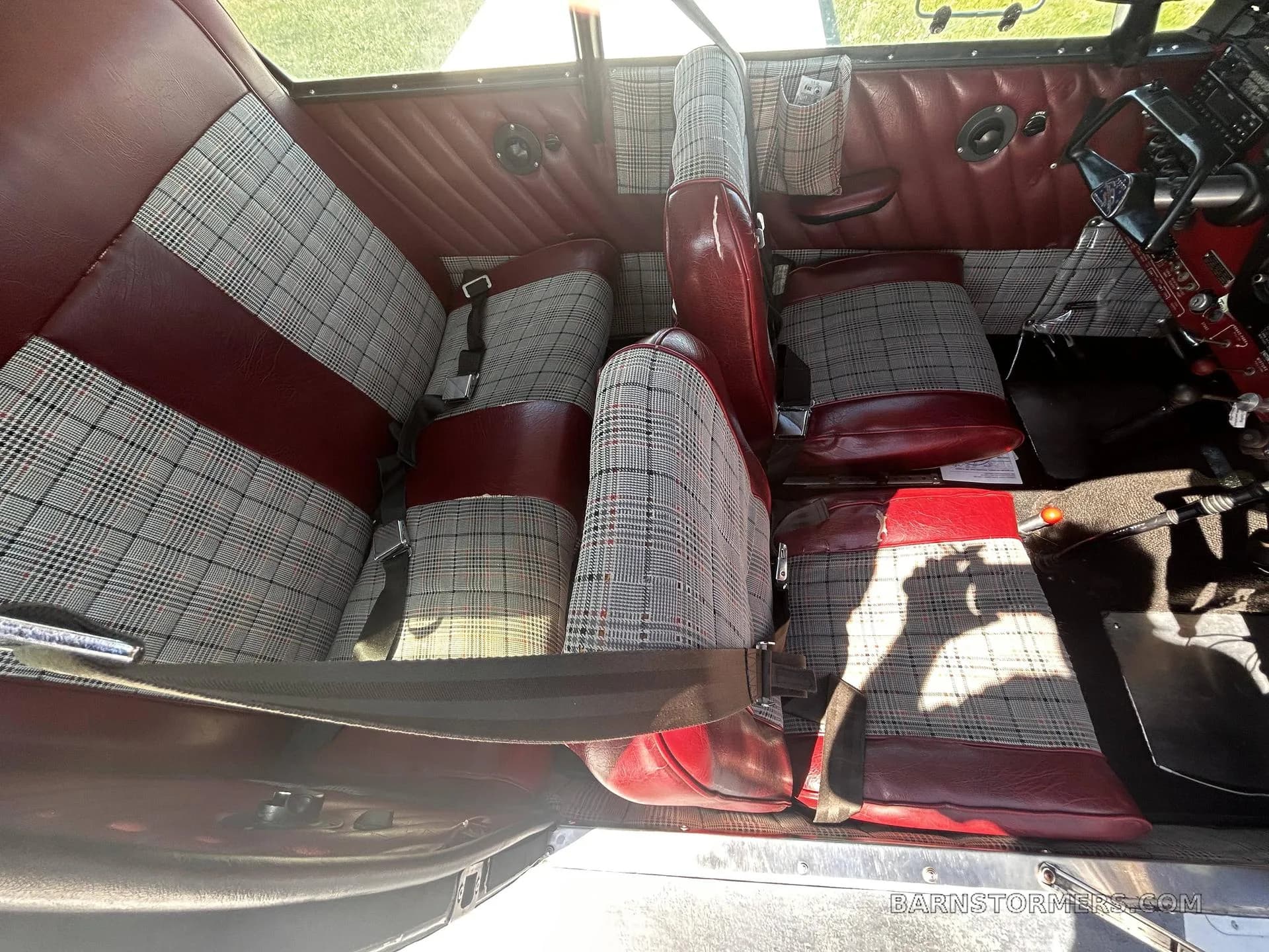 The aircraft's interior features red leather and plaid fabric seats, with seatbelts visible.