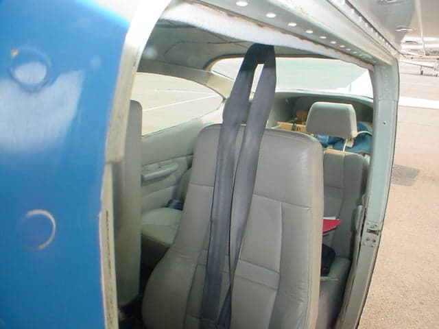 The light gray interior cabin of a small aircraft, viewed from the open door, showing the rear seats and seatbelts.