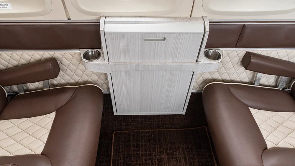 An overhead view of a folded aircraft table with cup holders between two brown and beige seats.
