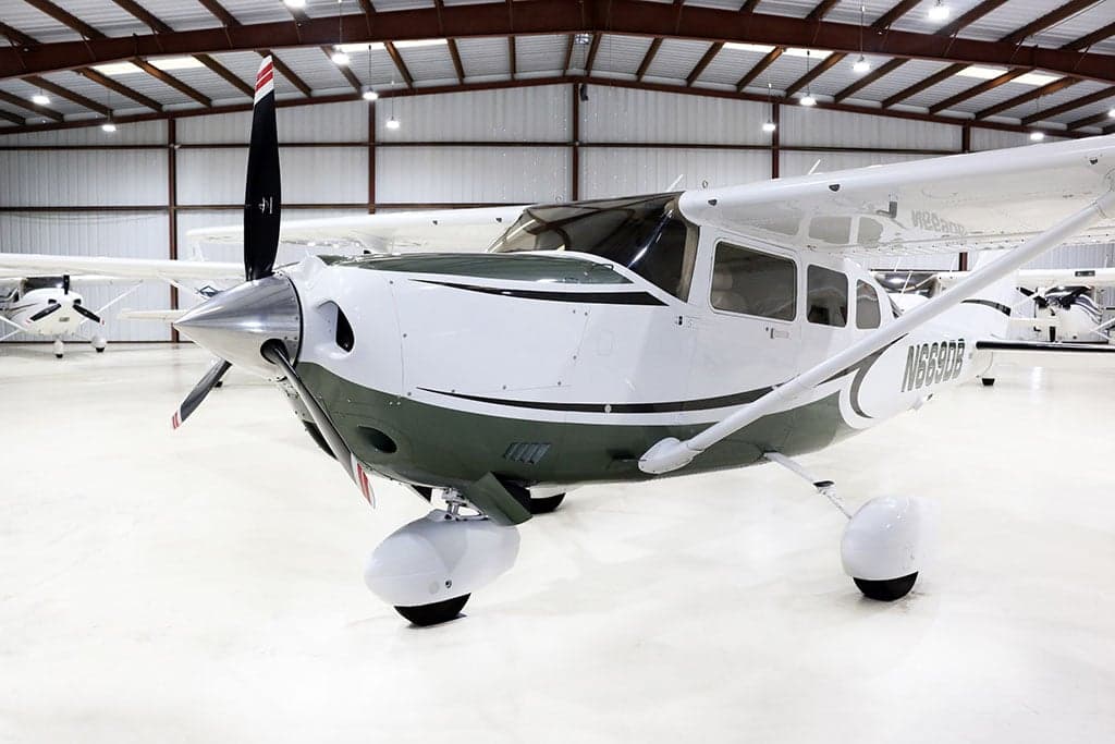 Three-quarter front view of a white and green Cessna Stationair TC, registration N669DB, parked in a hangar.