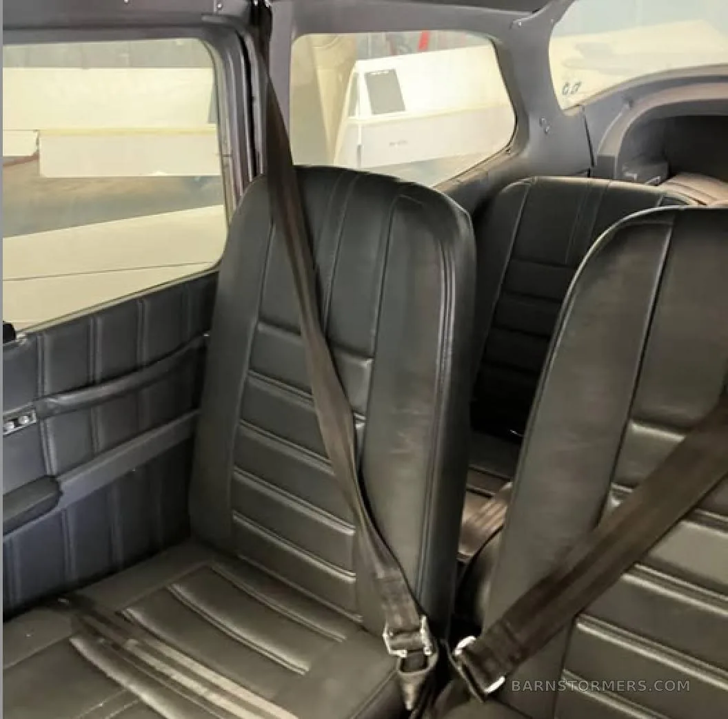 The interior cabin of an aircraft showing two rows of black leather seats with seatbelts.