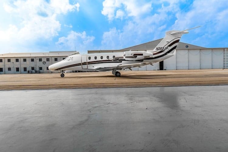 A Cessna Citation VII, tail number N202JP, parked on the tarmac in front of a hangar.