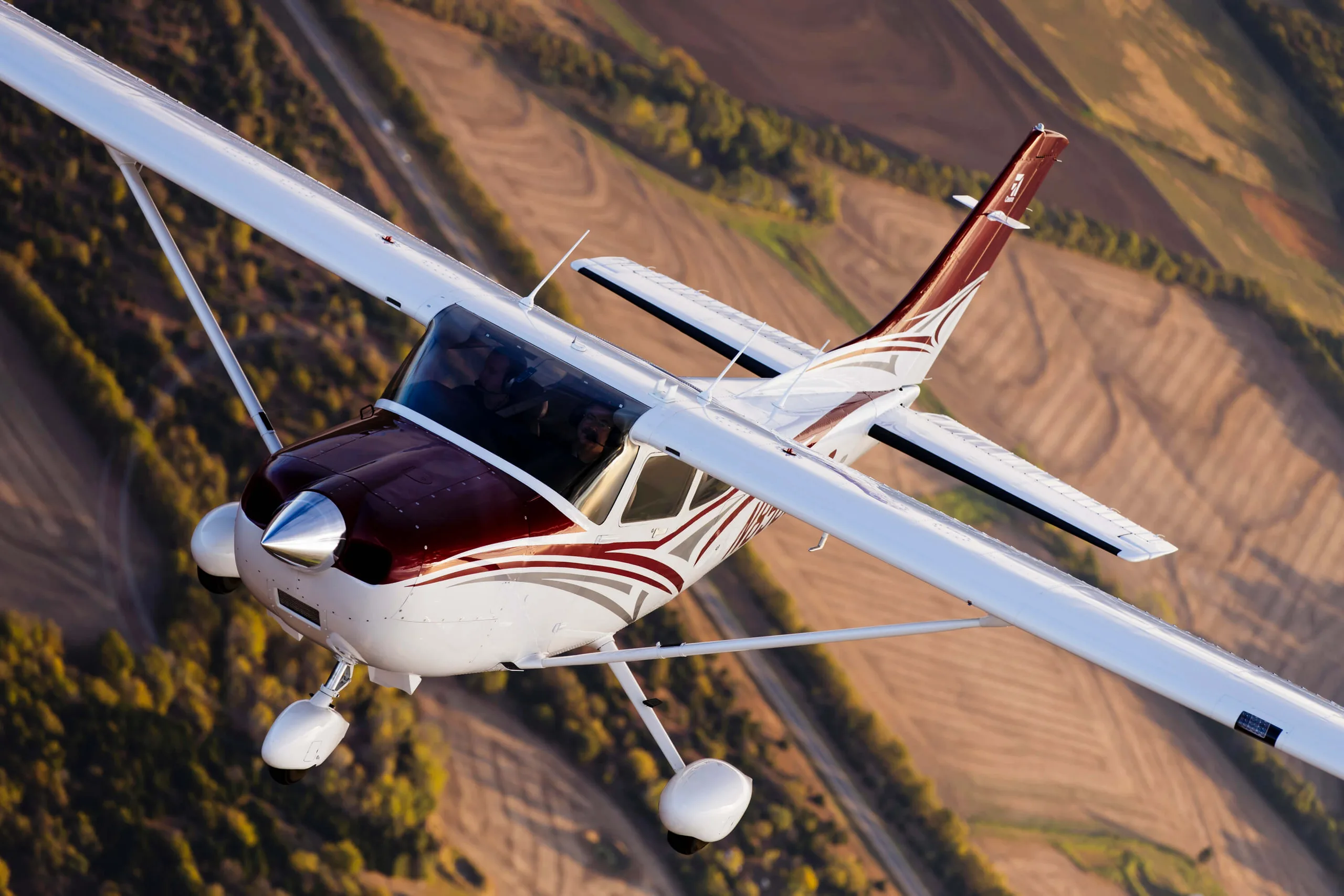 A Cessna 206 Stationair in flight over a rural landscape, showcasing its distinctive maroon and white paint scheme.