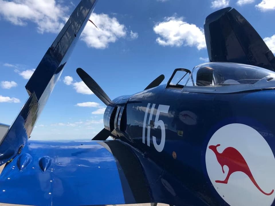 A blue aircraft parked on the tarmac with its wings folded, showing the tail number F-AZXJ.