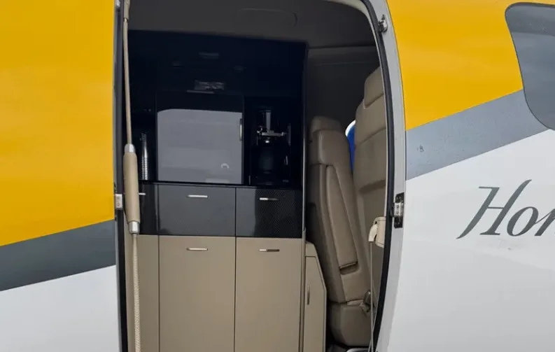 A close-up view of the refreshment center inside a HondaJet Elite, featuring a microwave and coffee maker, seen through the open main cabin door.