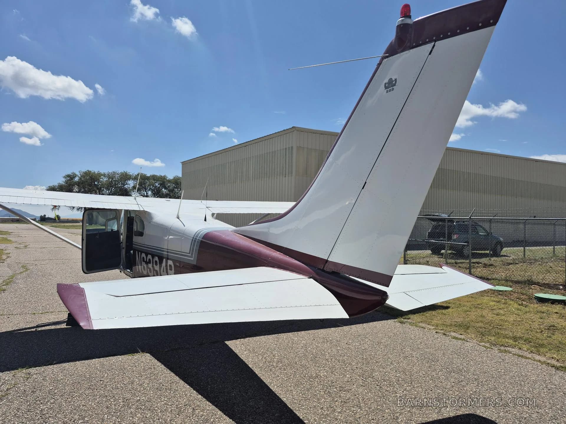The rear view of a red and white single-engine propeller aircraft (N6394B) with its door open, parked on an airfield.