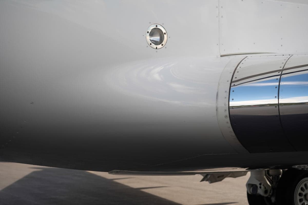A close-up view of the polished engine cowling and fuselage of a white business jet on an airfield.